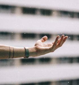 photograph of an arm reaching into the sky to feel the rain in the palm of their hand