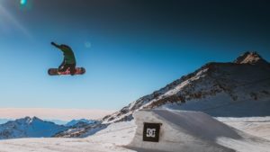 Snowboarder grabbing board while in the air after going off a jump. 