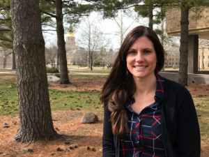 Photograph of Erika Hosselkus, taken outside the Hesburgh Library, with the golden dome of the Notre Dame administration building visible in the background.