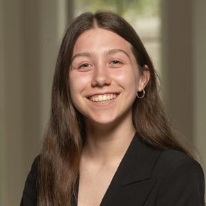 Headshot of Anna Schloss, SWE Recruitment Co-Director, wearing a black blazer, smiling in front of a softly blurred indoor background.