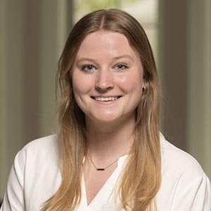 Headshot of Emily Norton, SWE Membership Enrichment Chair, wearing a white blouse, smiling in front of a softly blurred indoor background.