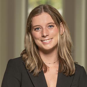 Headshot of Kylie Brewster, SWE External Outreach Chair, wearing a black blazer and black top, smiling in front of a softly blurred indoor background.