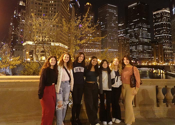 Group of seven SWE members posing together on a bridge at night with illuminated skyscrapers in the background, enjoying an evening in the city.
