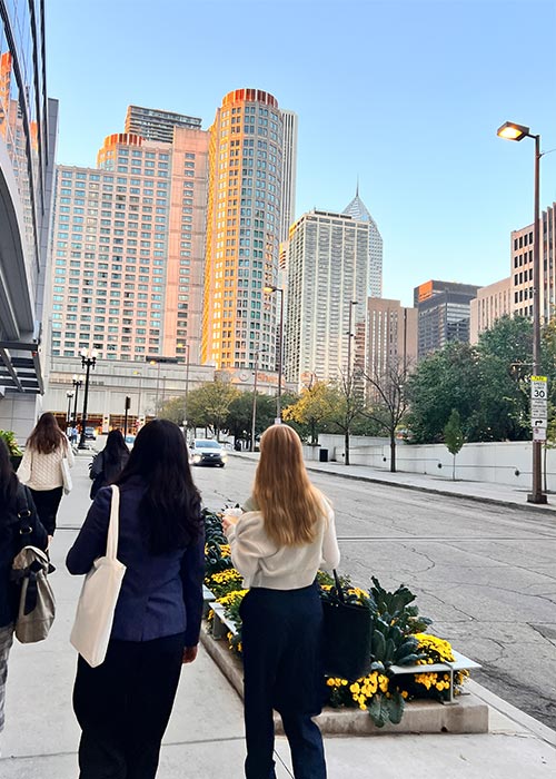 SWE members walking through a city street during the day, with tall buildings and flower planters visible along the sidewalk under a clear blue sky.