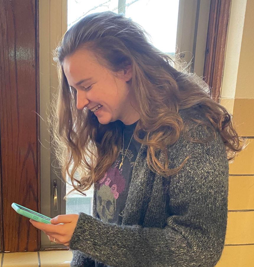 Female in her early twenties viewing her phone with a smile. 