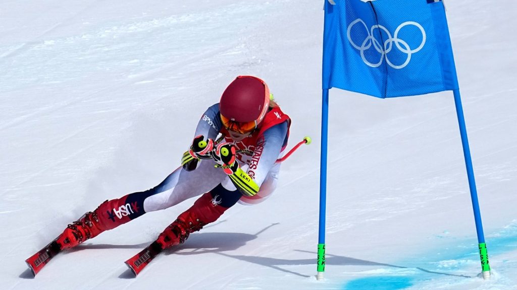 Photo of Mikaela Shiffrin, a world champion ski racer, in a low tuck position. She is turning around a blue gate racing in the 2022 winter Olympics. 