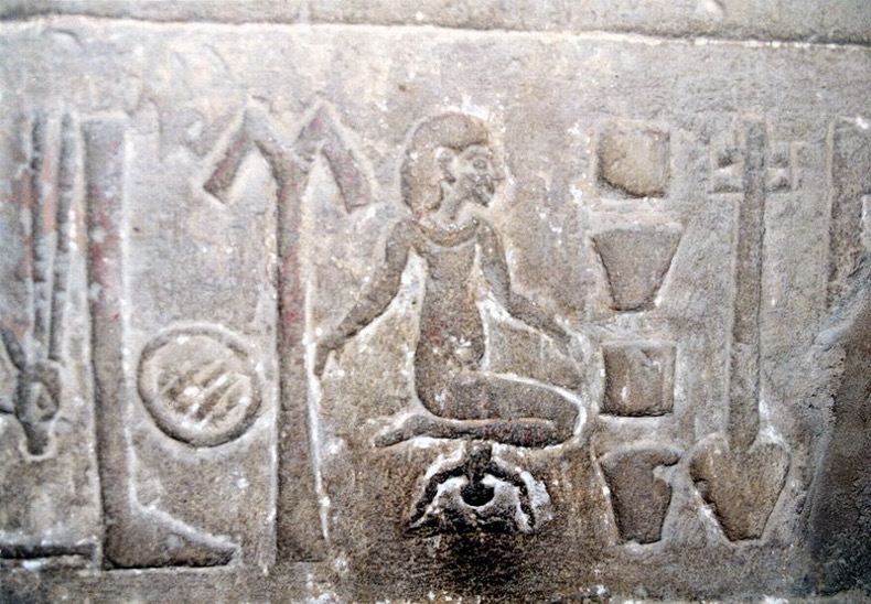 An ancient Egyptian relief depicts a stone carving of a women giving birth from a kneeling position, with the child shown beneath her.