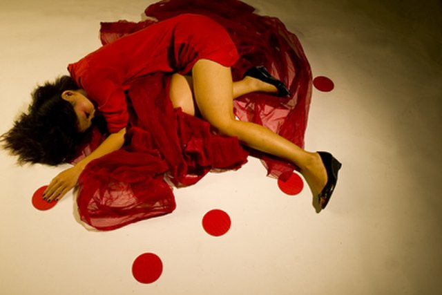 the image shows a woman in a red dress laying on the ground with knees bent in depiction of period pain