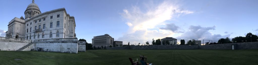 A large state house overlooks an empty green space during the sunset.