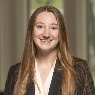 Portrait of Sarah Eginton, Co-Treasurer of Notre Dame SWE, wearing a white blouse and black blazer, smiling in front of a blurred indoor background.