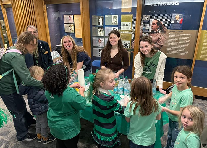 SWE members engaging with a group of young children at an outreach event, gathered around a table with hands-on activities in front of display cases.